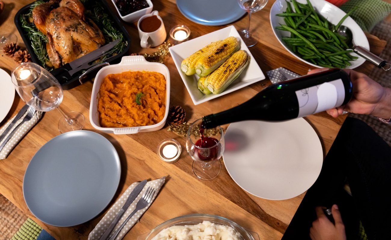 High angle view of a young mixed race man sitting at a table at home set for Thanksgiving dinner pouring a glass of red wine from a bottle best wine